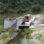 Lake weed removal machine collecting aquatic vegetation from water surface